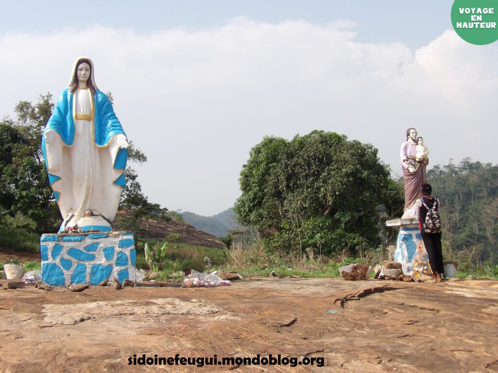 Statuette de la Vierge Marie au second palier du Mont Béatitudes. En arrière-plan le versant arrière du Mont Ebaminala.  Crédit : Sidoine FEUGUI